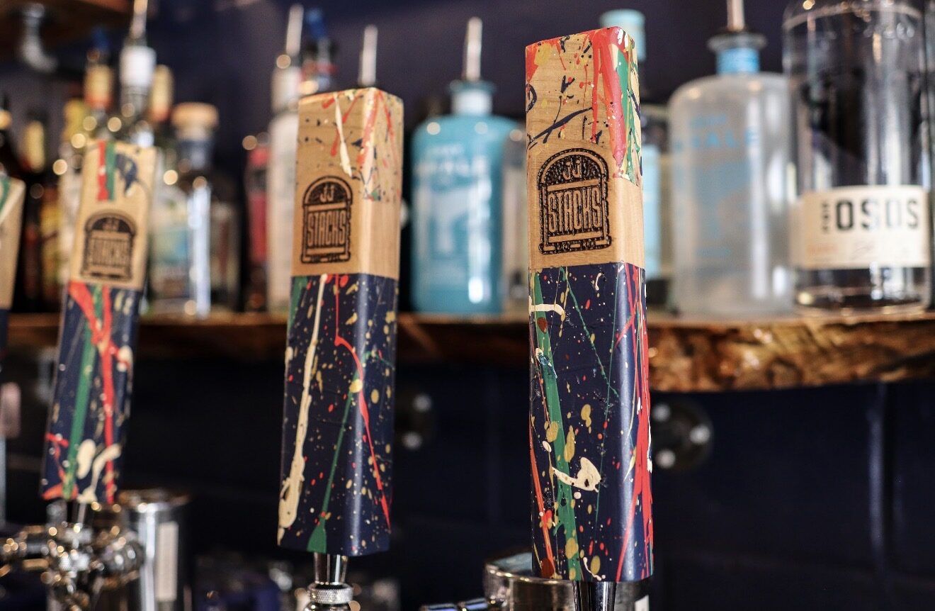 JJ Stacks tap handles at the bar, paint-splattered and hand-branded