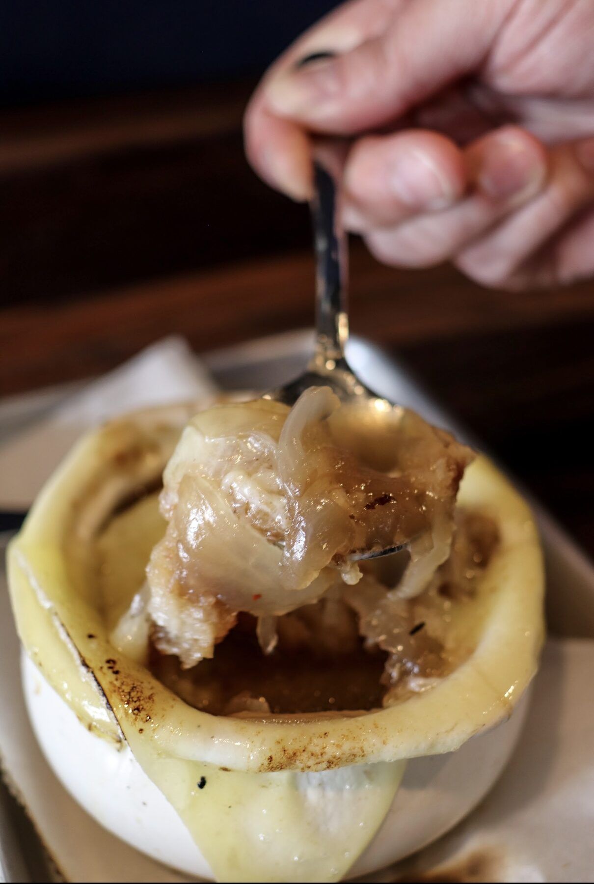 Spoonful of melted cheese and caramelized onions lifted from the French onion crock