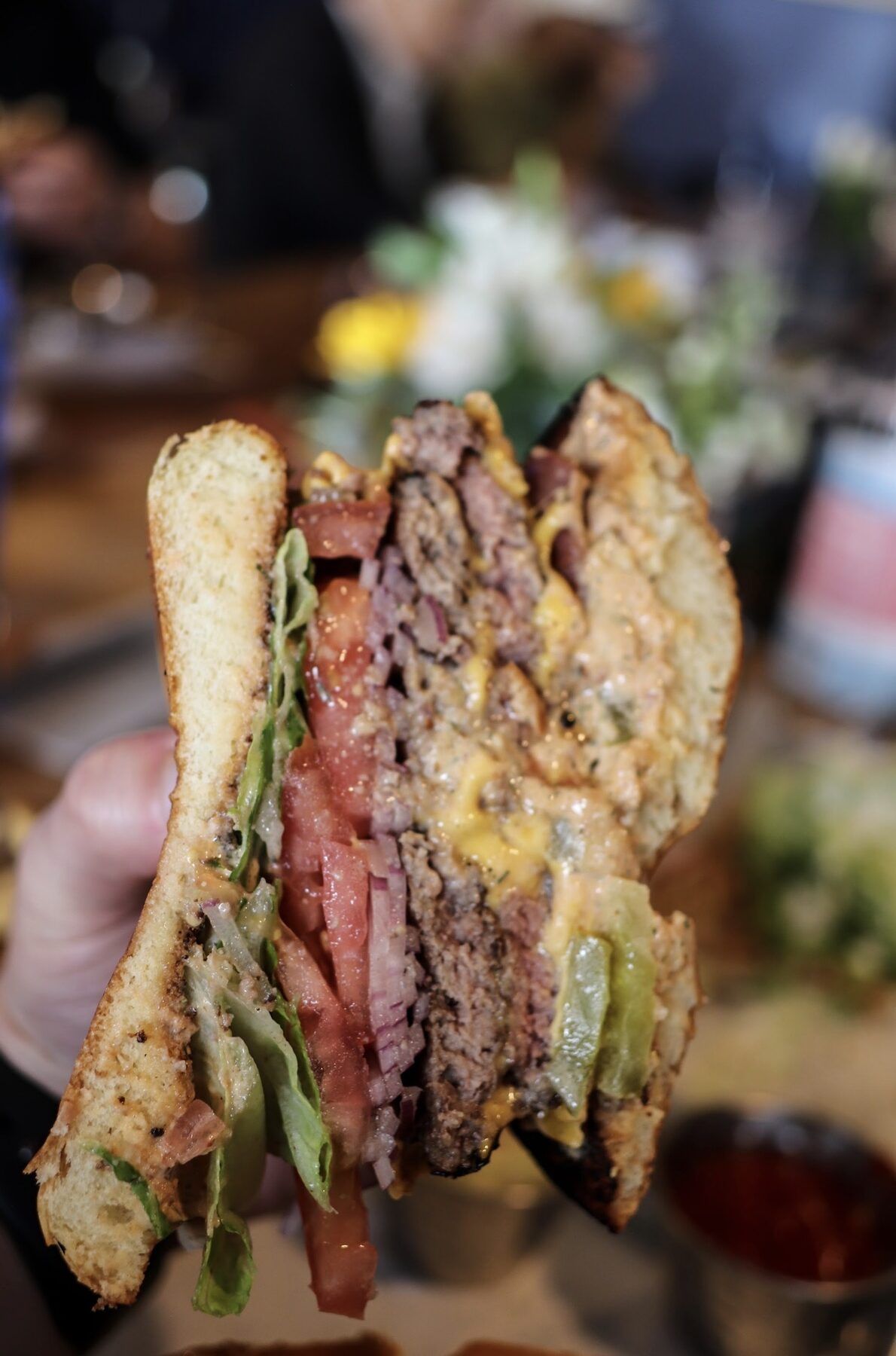 A Stack cut in half — double patty, American cheese, bacon, lettuce, tomato, and pickles on toasted brioche