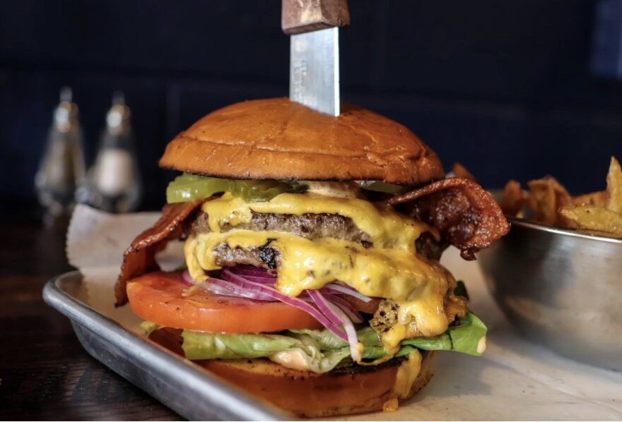 Dining room — gold-framed burger painting on a navy brick wall, industrial chairs at small wood-top tables